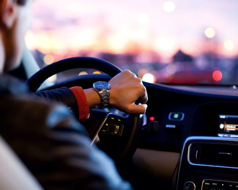 A driver on the road at dusk with hands on the steering wheel
