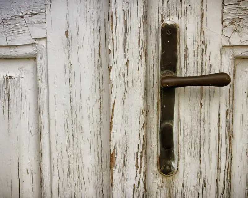 An old lever handle and keyhole on a weathered wooden door